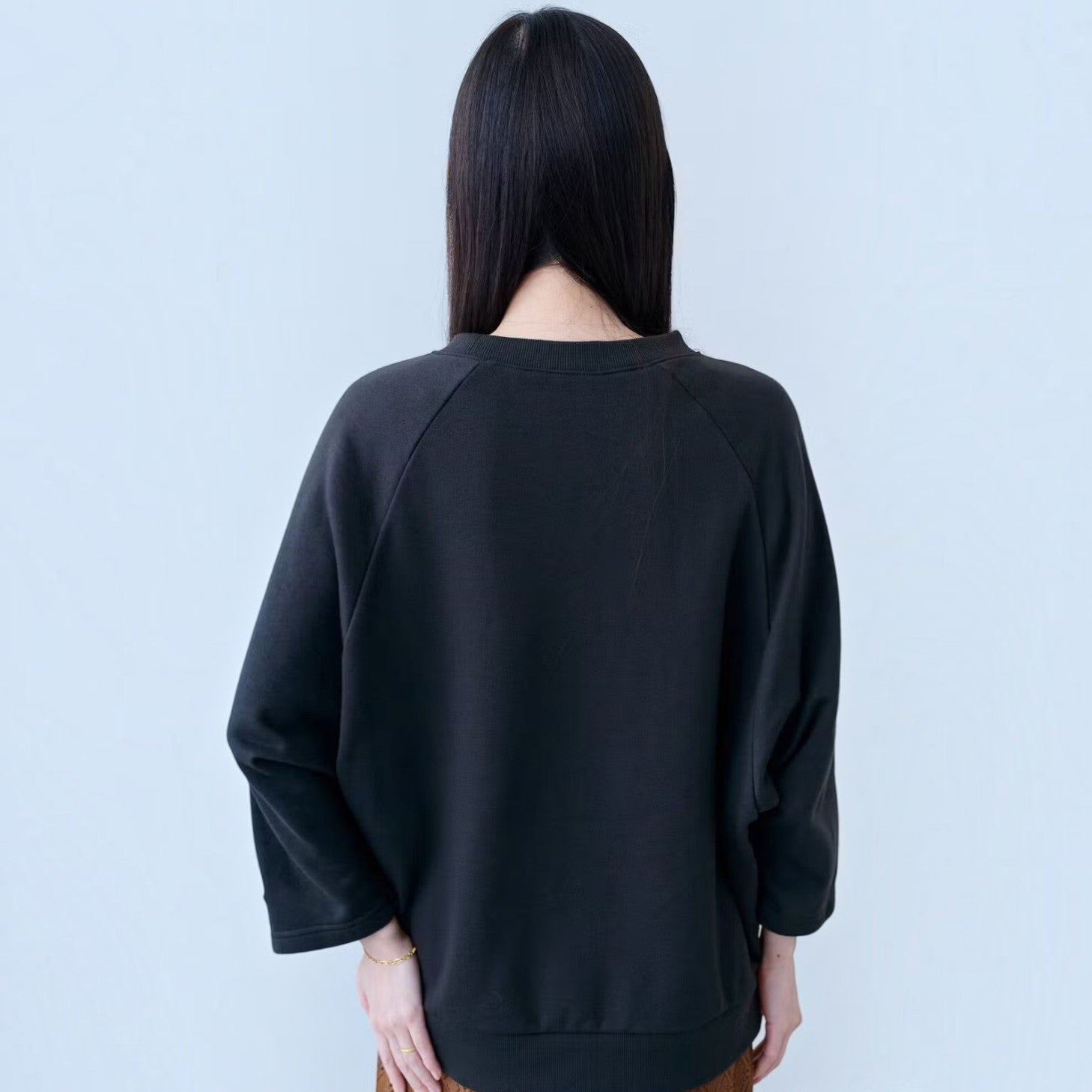 Back view of a woman wearing a charcoal black hibino Cooperstown Collection sweatshirt with three-quarter sleeves.